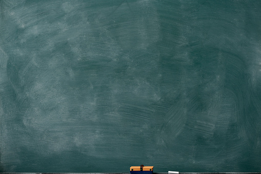 Close-up of smudged blank blackboard with board eraser and chalk.