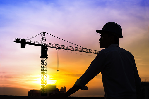 portrait of architect silhouette wear a helmet at construction site with crane background and sunset