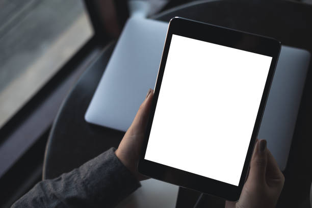 istock Top view mockup image of woman's hands holding black tablet pc with blank white desktop screen with laptop on table in cafe 918786198