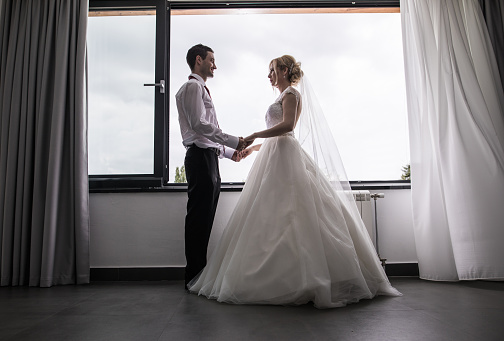 Low angle view of happy newlyweds holding hands by the window and communicating.