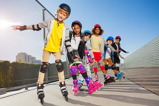 Group of multiethnic boys and girls, in-line skaters, standing one after another outdoors in summer