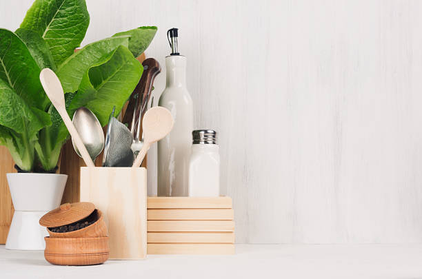 Kitchen white interior with wooden beige kitchenware, spices, ceramics and green spinach bush on light wood board, copy space.