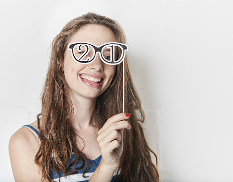 A cute girl smiles as she tries on fancy-dress eyeglasses with the number 21 in place of lenses, ready for a 21st birthday party.