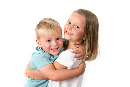 A brother and sister are hugging each other and are smiling and looking at the camera.