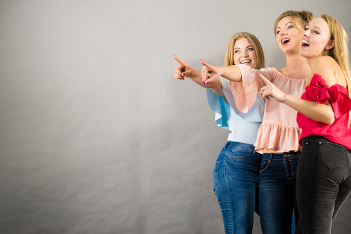 Fashionable adult female friends models pointing at grey copy space. Studio shot