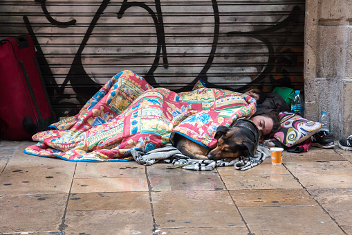 BARCELONA, SPAIN, February 4, 2018 A young guy, a girl and a dog covered with blankets sleeping on the street in the rain.