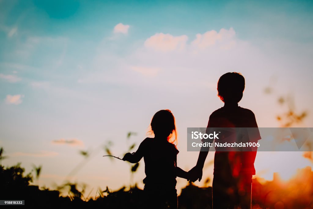 little boy and girl silhouettes holding hands at sunset little boy and girl silhouettes holding hands at sunset nature Brother Stock Photo