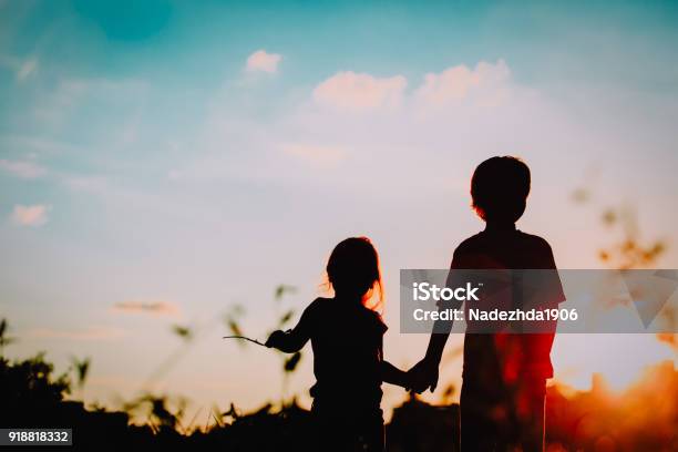 Little Boy And Girl Silhouettes Holding Hands At Sunset Stock Photo - Download Image Now