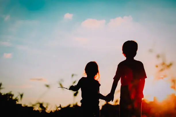 Photo of little boy and girl silhouettes holding hands at sunset