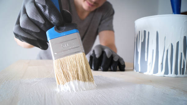 nahaufnahme: pinsel mit weißer farbe auf einem holztisch und ein glas mit farbe - anstreicher stock-fotos und bilder