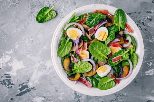 lunch bowl of spinach salad with bacon, mushrooms, eggs and red onions lunch bowl of spinach salad with bacon, mushrooms, eggs and red onions on gray background quail egg stock pictures, royalty-free photos & images