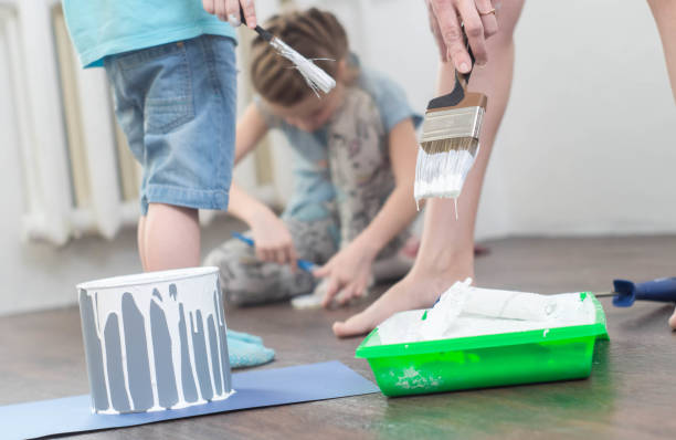 istock Children help in repairs: a boy and a girl dunk brushes and a roller into white paint 918824736