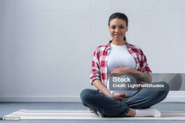 African American Pregnant Woman Sitting On Yoga Mat Stock Photo - Download Image Now