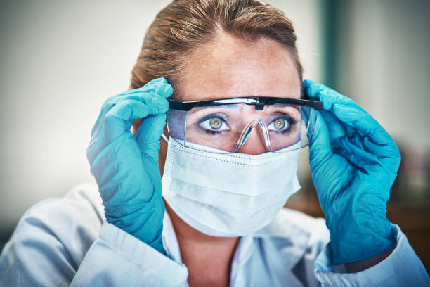 istock Female scientist in mask and goggles stares seriously 918825950