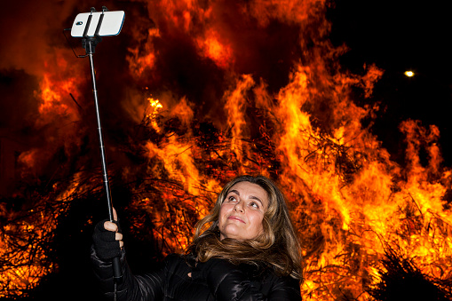 Attractive woman takes a selfie in front of a big fire during a nighttime village festival