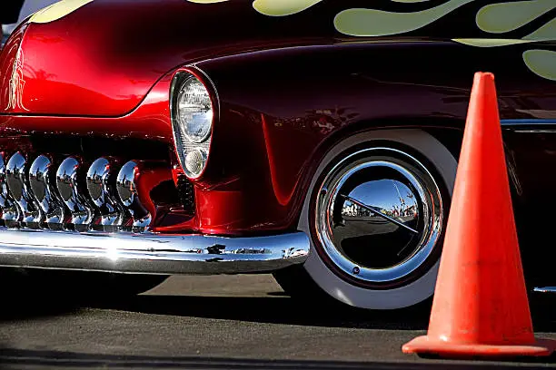 A cropped image of a fully restored classic old car with lots of shiny chrome. This image includes a bright orange traffic cone.
