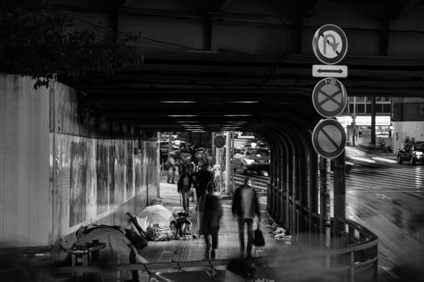 Tokyo, Japan - October 29, 2017: City in the Rain - indifference as people walk pass the homeless sheltering under a railway bridge during a torrential downpour. Black and white