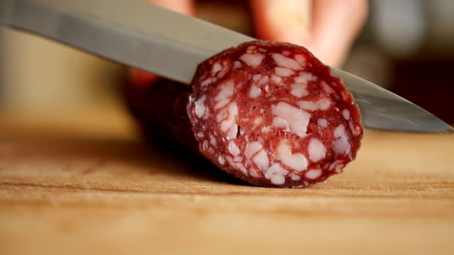 Man cuts into thin slices fatty sausage. Shooting closeup. Chef cutting salami with a knife on a wood board close up.