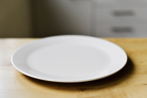 closeup of an empty white ceramic plate on a modern wooden table or countertop