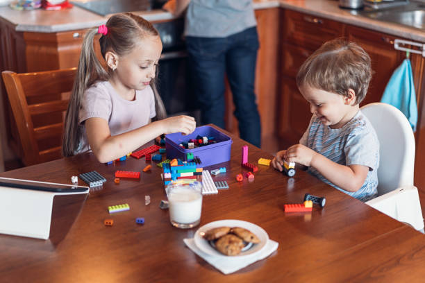 Two young children playing together with colorful building blocks and having some snacks.