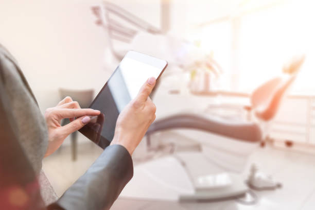 Manager of dental clinic Horizontal color image of female hands holding digital tablet, dentist's chair and dental equipment. tablet pc and digital hospital tools stock pictures, royalty-free photos & images