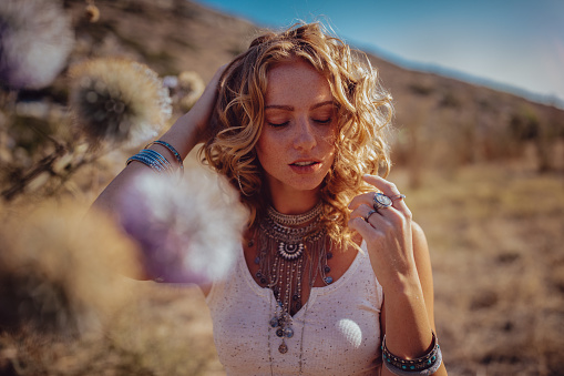 Young woman in boho style with freckles, silver jewelry and wavy hairstyle daydreaming in field