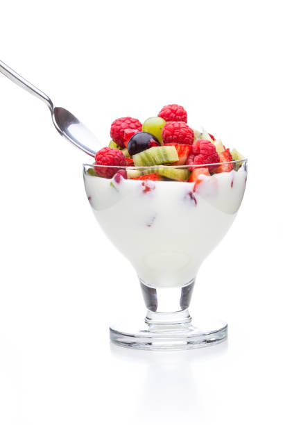 Spoon dipped in yogurt with several different kinds of fruit