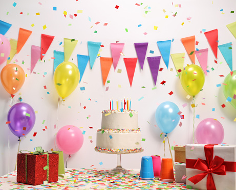 Birthday cake on a table against a wall with decoration flags and balloons