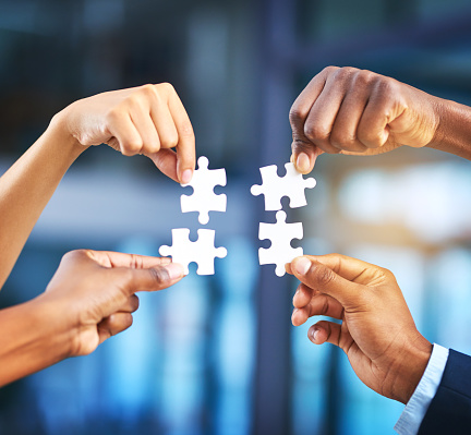 Cropped shot of a group of businesspeople completing a puzzle together in a modern office