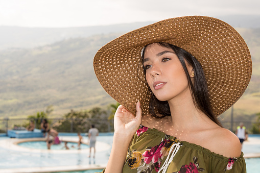 Portrait of young lady outdoors while she is holding a big hat looking away