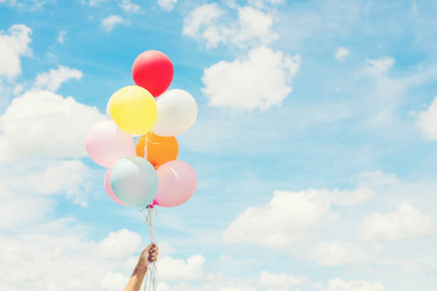 concepto de estilo de vida de mujer: mano mujer sosteniendo un manojo de globos de colores con el cielo azul. - child balloon happiness cheerful fotografías e imágenes de stock