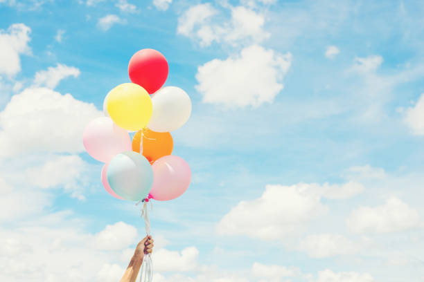 Woman Lifestyle concept : woman hand holding a bunch of colored balloons with blue sky. stock photo
