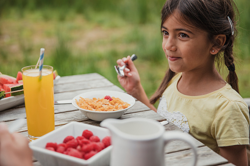 Little girl smiling as he eats her cereal outside.