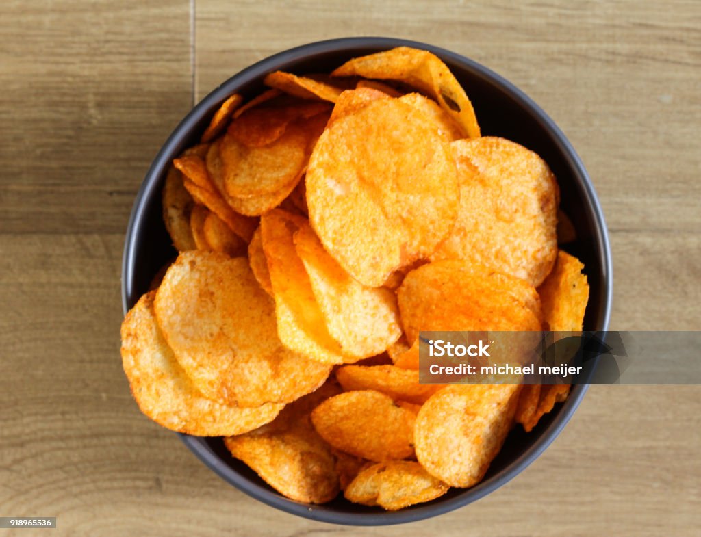 Spiced paprika Potato chips in a bowl on a wooden background close up of bowl with paprika chips on kitchen table Appetizer Stock Photo