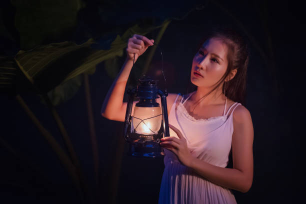 woman with vintage lantern outside at night - cosplay girl in nutral  costume holding a lamp, young woman in white long dress walking in night wood - nutral imagens e fotografias de stock