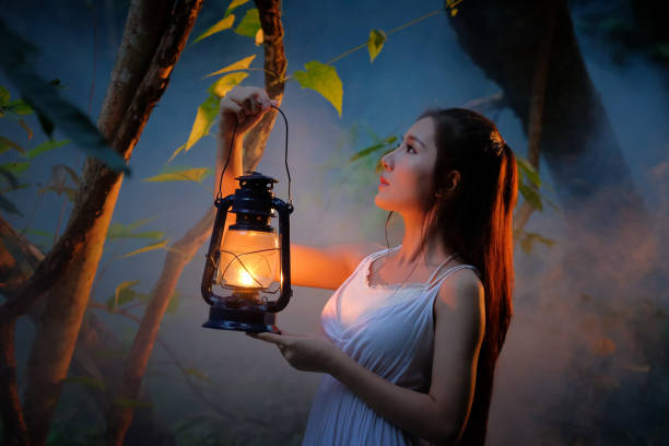 woman with vintage lantern outside at night - cosplay girl in nutral  costume holding a lamp, young woman in white long dress walking in night wood - nutral imagens e fotografias de stock