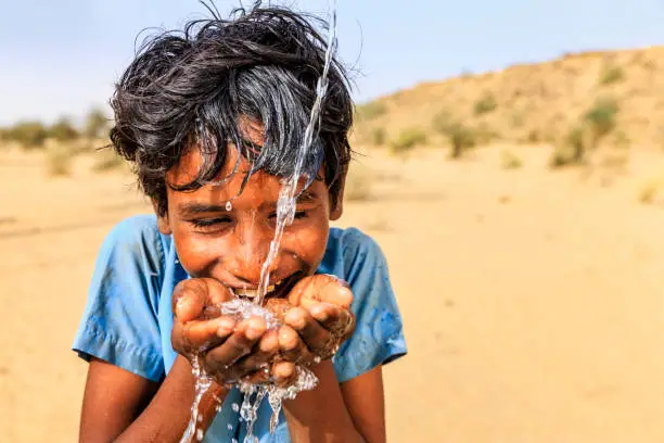 Indian young boy is drinking fresh water, desert village, Thar Desert, Rajasthan, India. Potable water is very precious on the desert - Rajasthani women and children often walk long distances through the desert to bring back jugs of water that they carry on their heads.