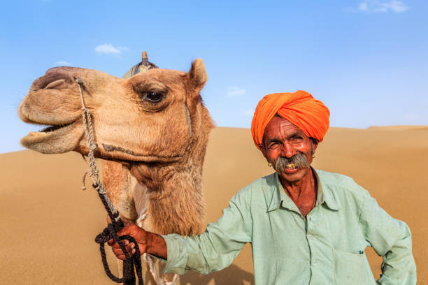istock Indian man holding camel on sand dunes, Rajasthan, India 918973578