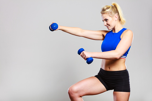 Sporty woman lifting light dumbbells weights. Fit girl exercising building muscles. Fitness and bodybuilding.