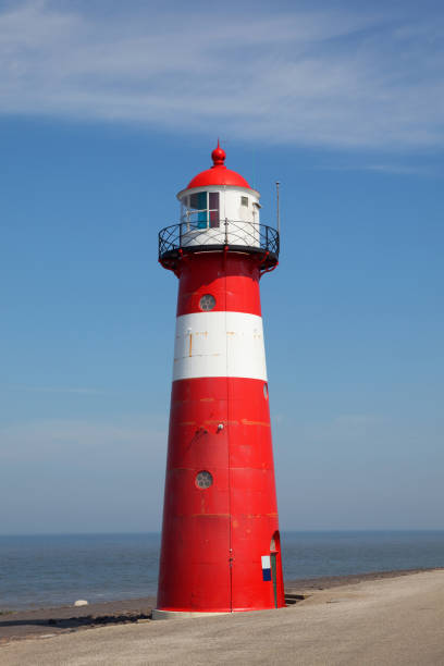 istock Red lighthouse on a dyke seawall by the blue sea 918989902