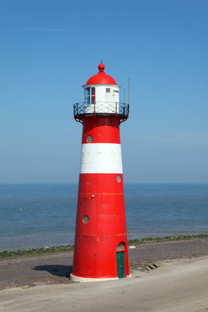 istock Red lighthouse on a dyke seawall by the blue sea 918989936