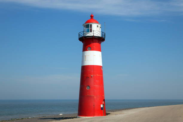 istock Red lighthouse on a dyke seawall by the blue sea 918989974