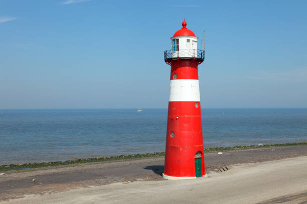 istock Red lighthouse on a dyke seawall by the blue sea 918989978