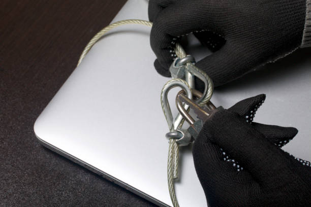 istock Computer security. Protection of access to data. The laptop is protected by a security cable and a lock. An attacker with gloves tries to open the lock and get access to the computer. 919131456
