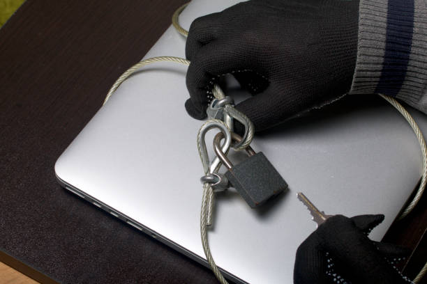 istock Computer security. Protection of access to data. The laptop is protected by a security cable and a lock. An attacker with gloves tries to open the lock and get access to the computer. 919131942