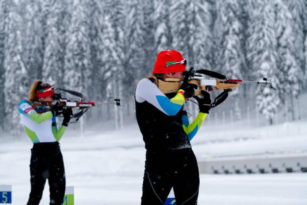 side view of two female athletes practicing target shooting in snowstorm - biathlon imagens e fotografias de stock