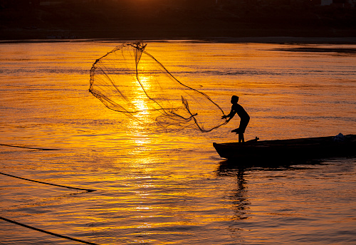 Katwa WB India - May 2, 2022: Taken this picture at river Ganges of a fisherman fishing using fishing lines. Tried to capture the flowing river at sunset in the summer season and people doing recreational fishing during vacation and livelihood.