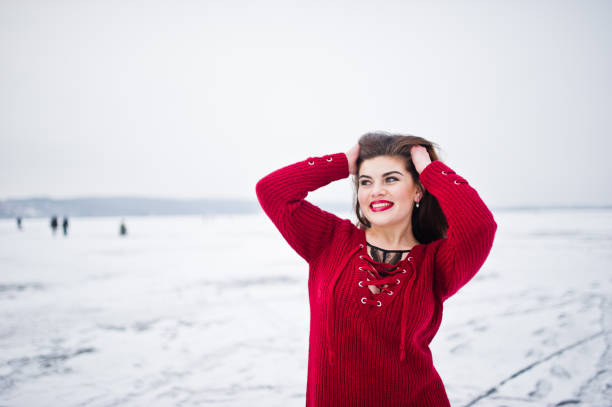 Brunette plus size model at red against frozen lake on winter day.