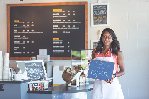Attractive African American coffeehouse owner holds up a sign 