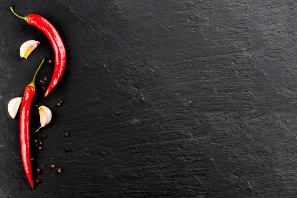 istock Red hot chili peppers and peppercorns on black background, top view with copy space 919338772